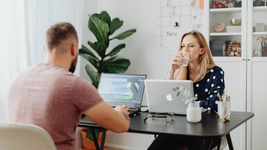 Two colleagues working in a stylish office space with laptops and beverages.